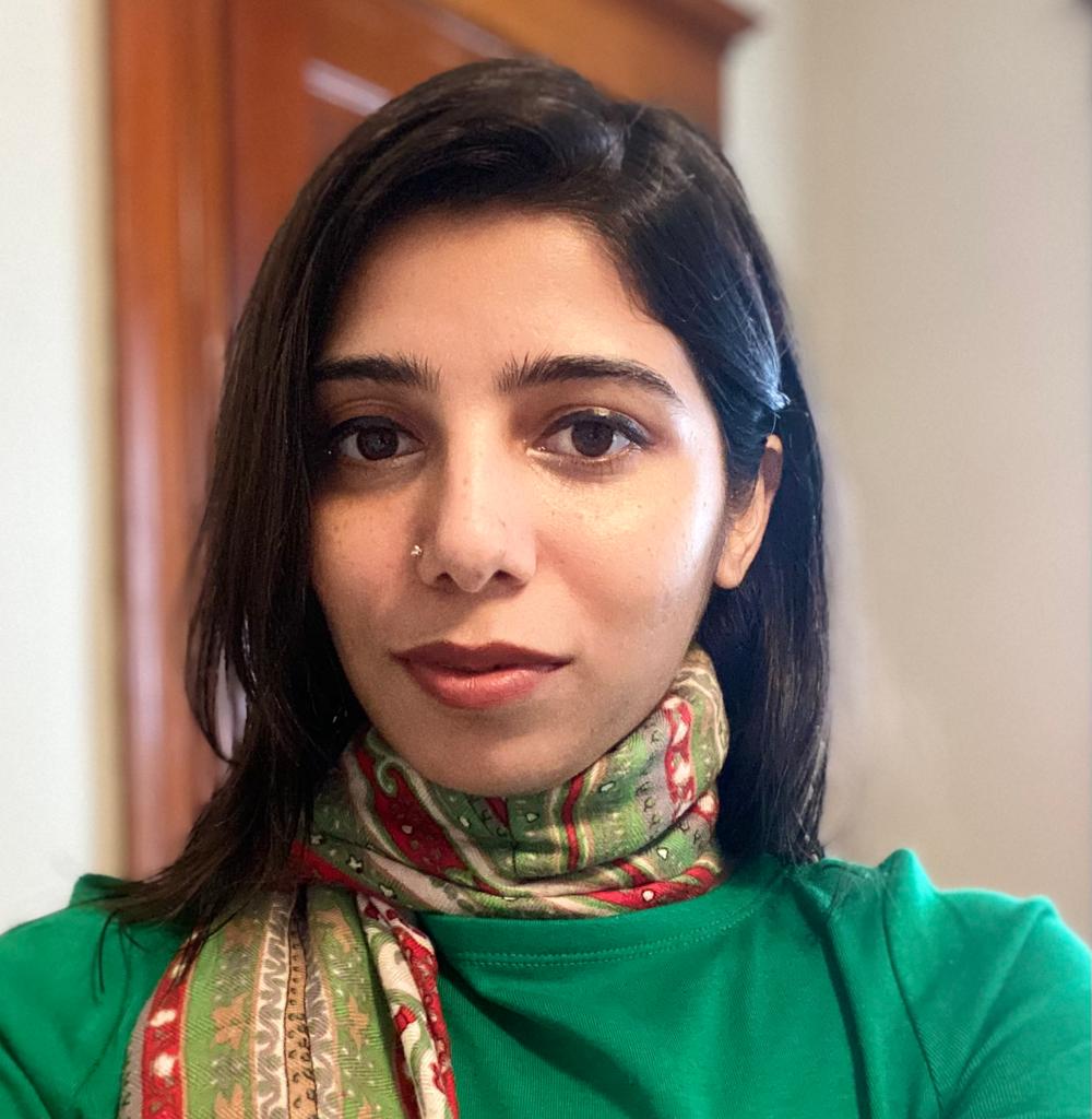 A female wearing a green top and a multi-color scarf around her neck.