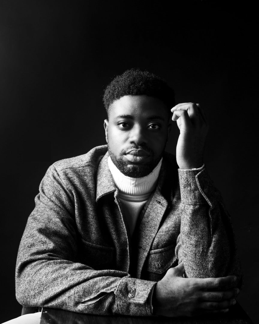 A boy is the dark wearing a black jacket and a white turtleneck