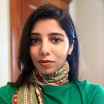 A female wearing a green top and a multi-color scarf around her neck.